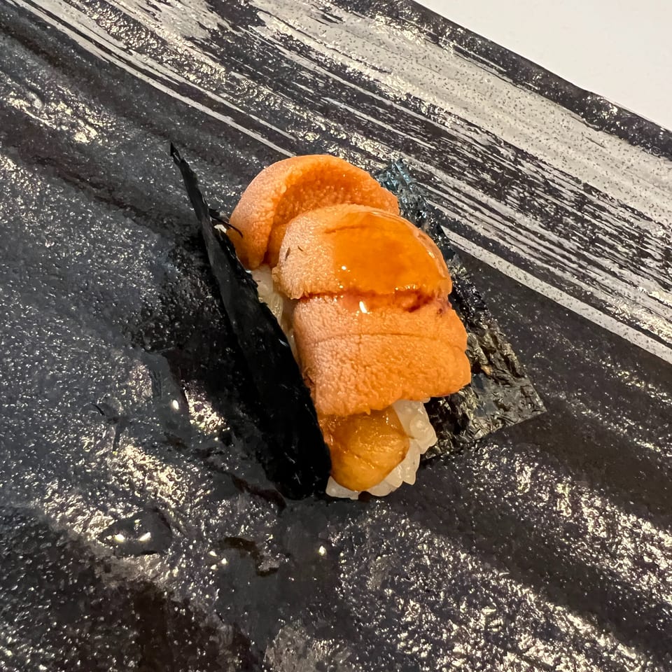 Close-up of orange salmon nigiri sushi on black slate, with white rice and glossy fish slices.