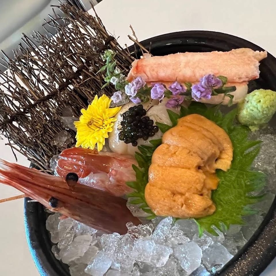 Japanese sashimi platter on crushed ice with sea urchin, shrimp, caviar, wasabi, edible flowers, and sea urchin shells.