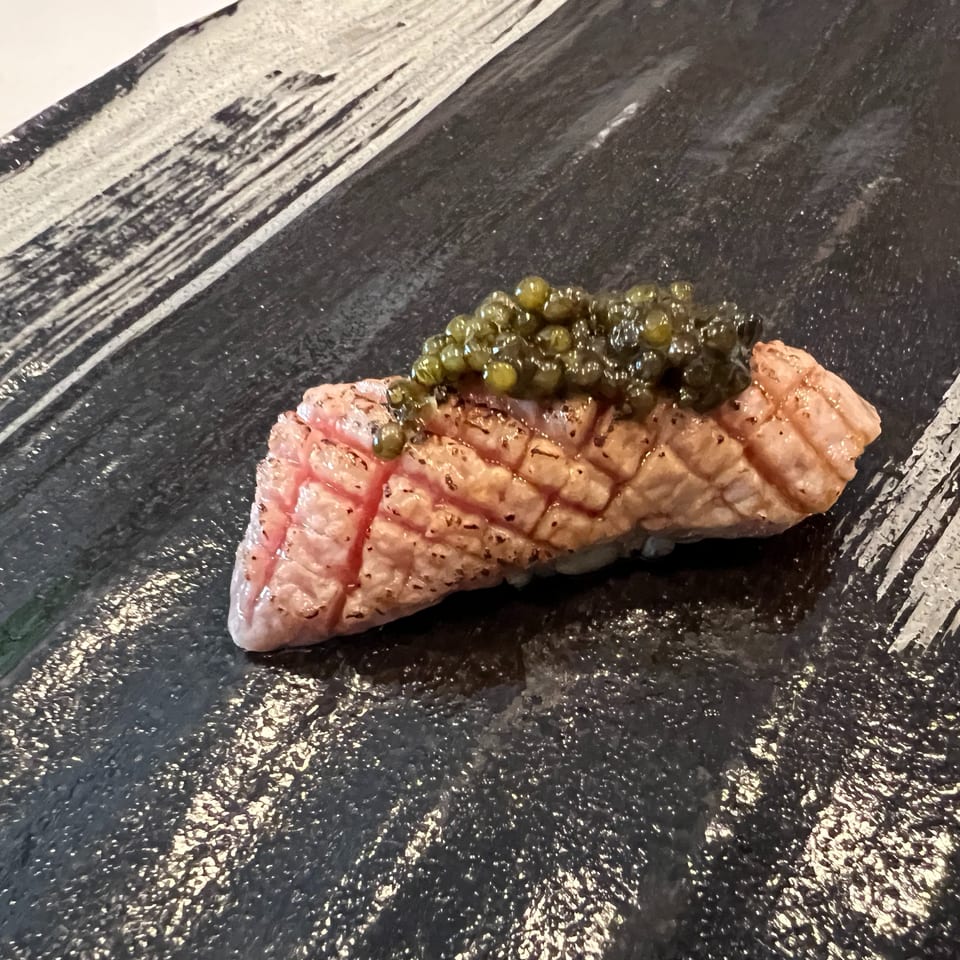 Seared tuna nigiri topped with green caviar on a black slate plate.