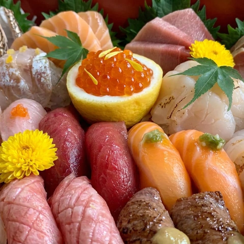 Close-up of an elaborate Japanese sushi assortment with assorted nigiri, sashimi, salmon roe, seaweed, and chrysanthemum garnishes.