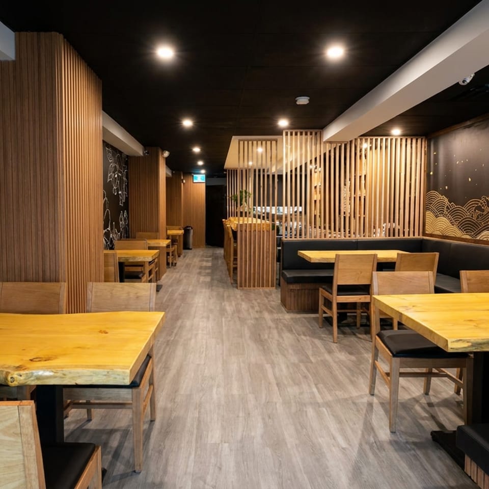 Modern restaurant dining room with wooden tables, black booths, floral wall art, wave mural, and vertical wood-slat partitions.